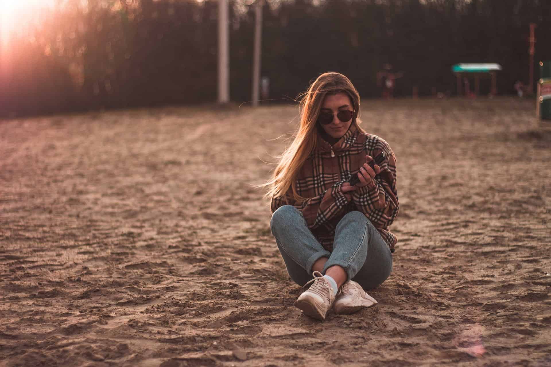 kvinnasammanträde på sandstrand som rymmer sin telefon