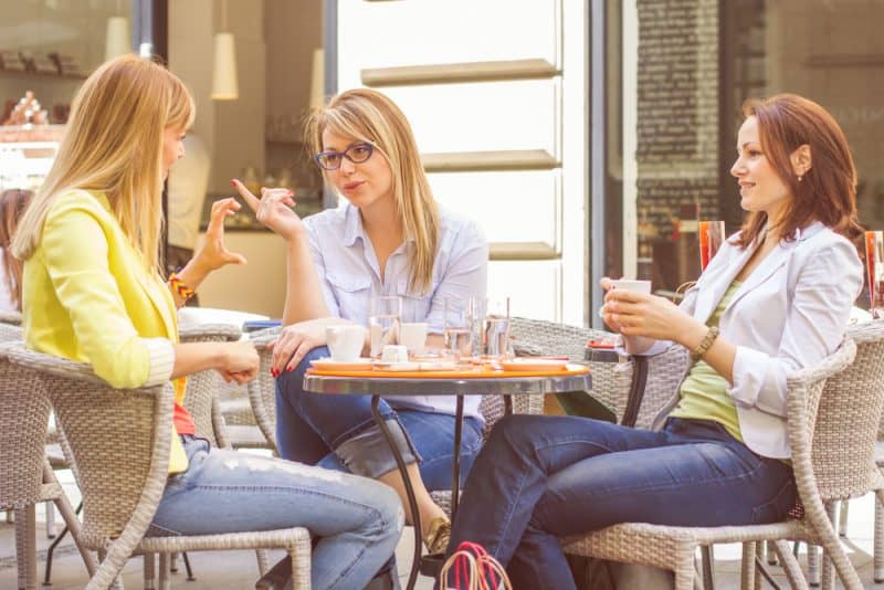 tre kvinnor som sitter vid bordet och pratar och dricker kaffe
