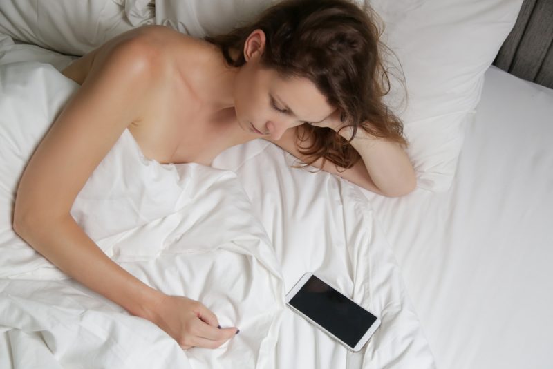 ledsen kvinna som ligger i sängen och tittar på sin telefon