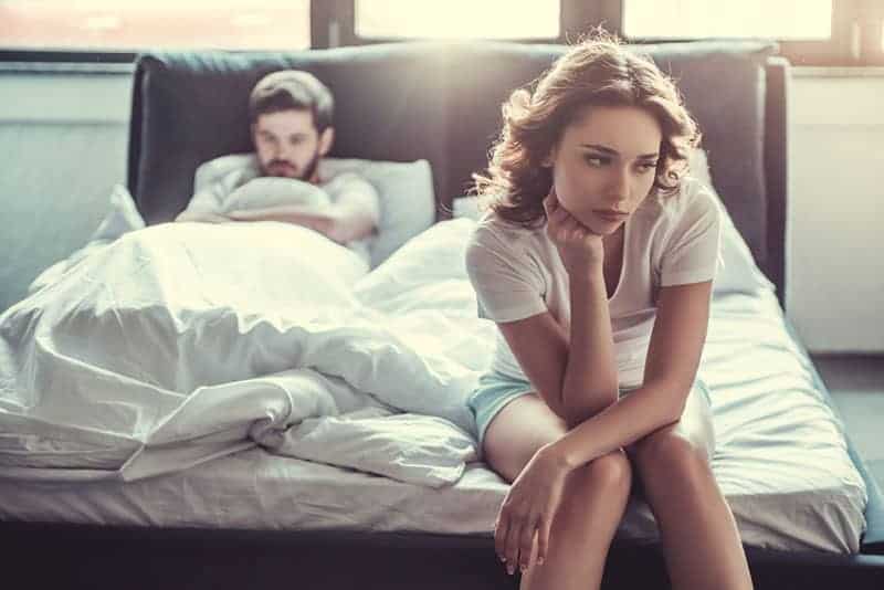 ledsen kvinna som sitter på sängen med mannen i bakgrunden