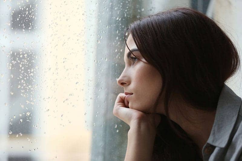 ledsen kvinna som tittar genom regnigt fönster