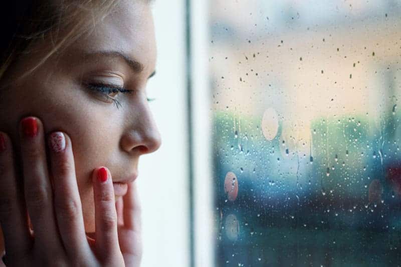 ledsen ung kvinna som tittar genom fönstret