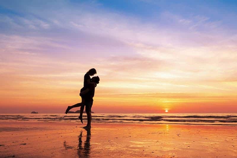 lyckliga par på stranden vid solnedgången