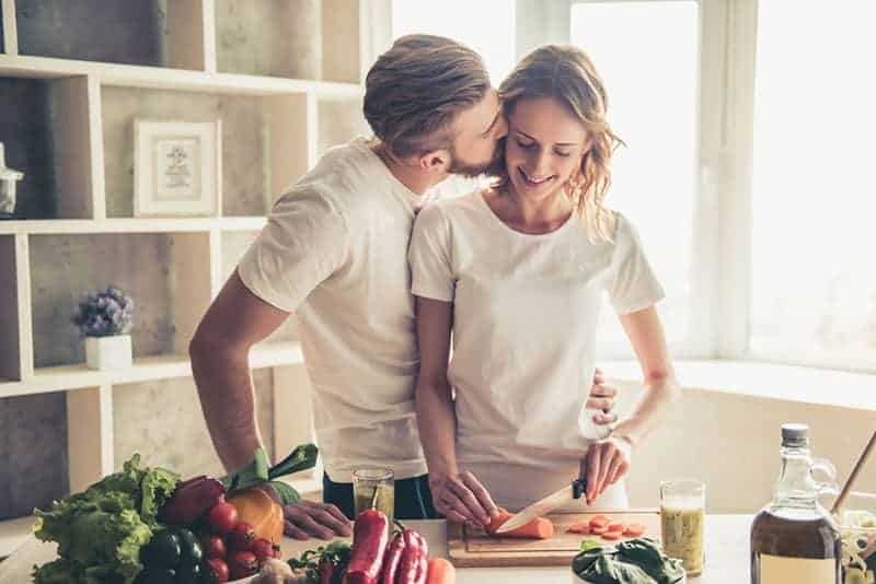 man kysser kvinna medan hon lagar mat