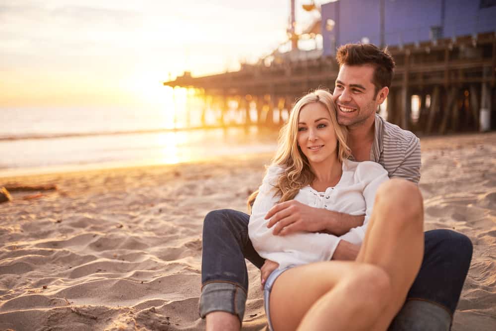 man och kvinna kramar på stranden i solnedgången