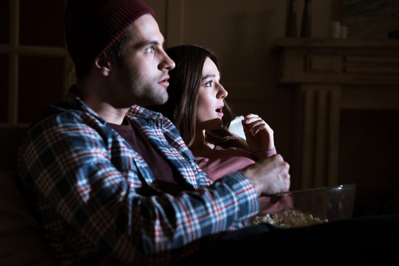 sidovy av chockade par tittar på film tillsammans hemma