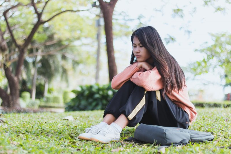 ung ensam kvinna som sitter på gräset i park