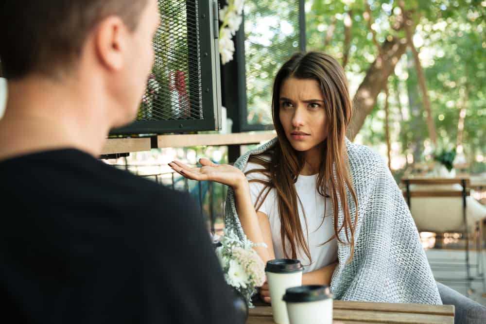 ung kvinna som gester med handen och tittar på sin pojkvän medan hon sitter på ett kafé