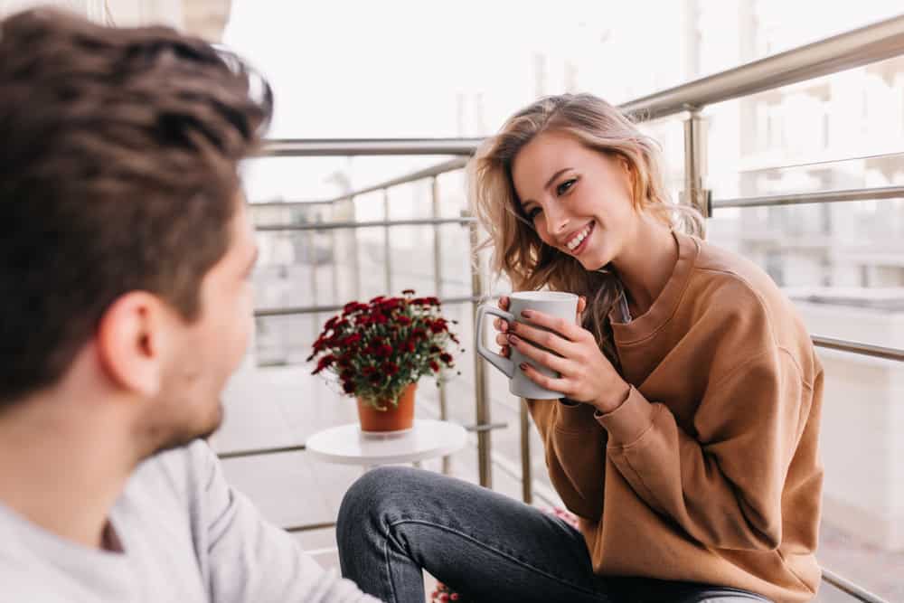 Bedövning flicka med lockig frisyr som dricker kaffe på balkongen med mannen