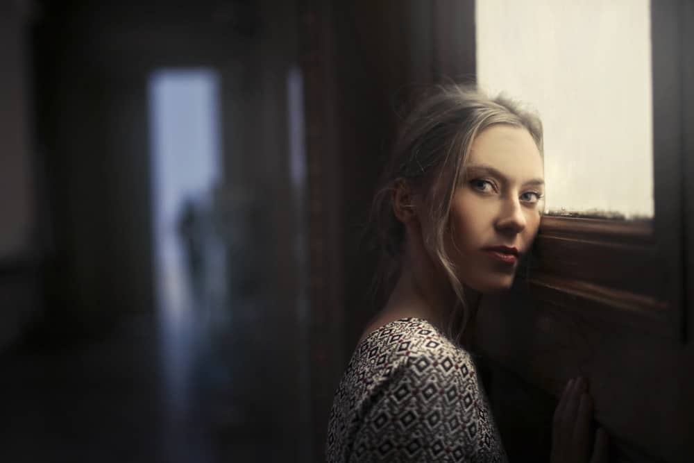 Blond kvinna som lutar mot en dörr med ett sorgligt uttryck