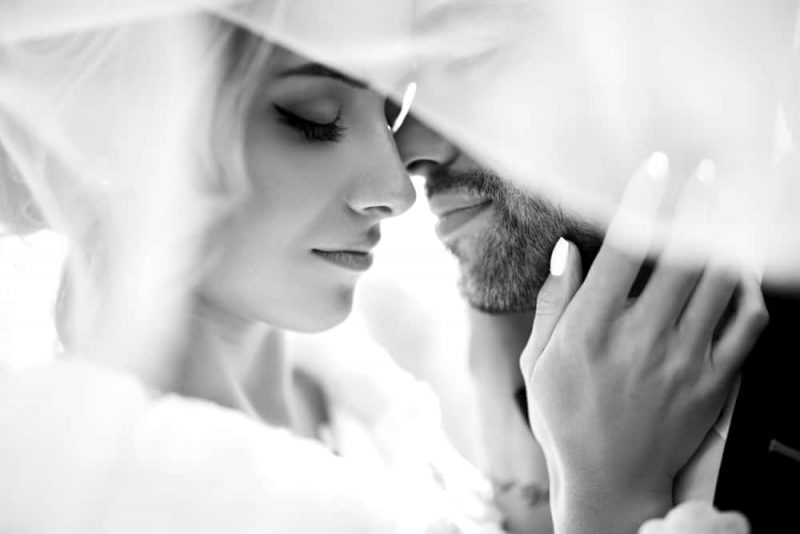 Bruden och brudgummen kyssar ömt i skuggan av en flygande slöja