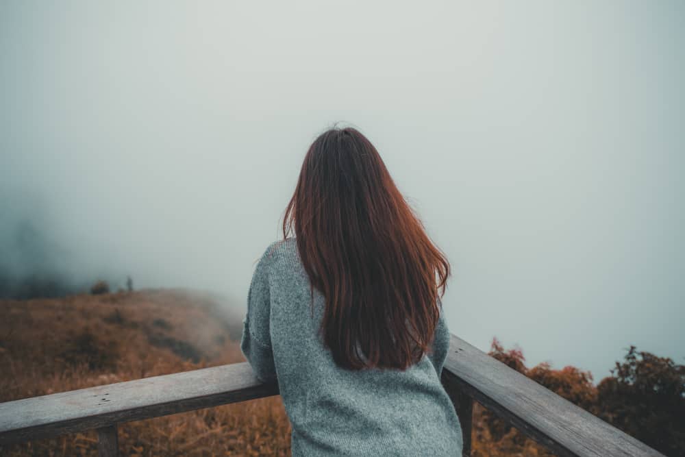 En kvinna som står ensam på balkongen som ser vit dimmigt och berg