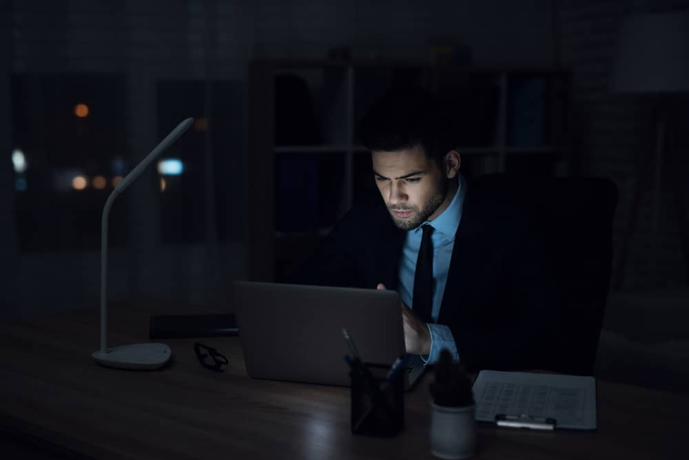 En man sitter på en bärbar dator i ett mörkt kontor