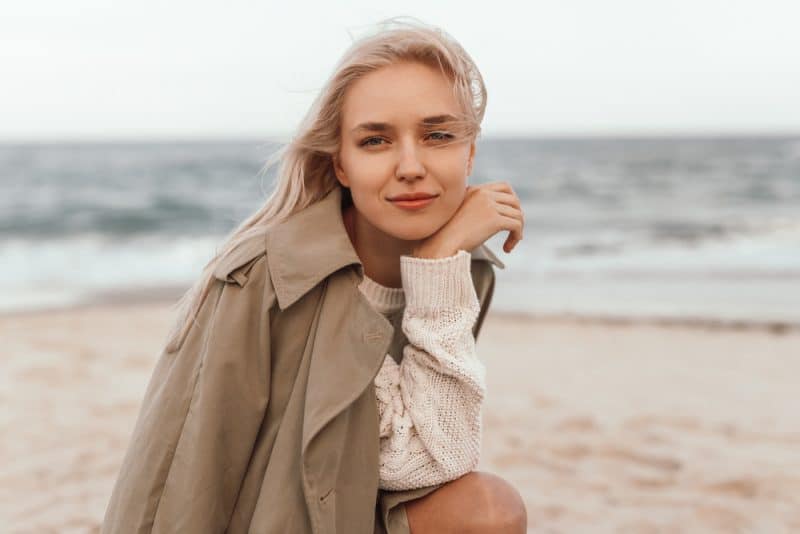 Lugn ung blond kvinna i varm tröja och kappa