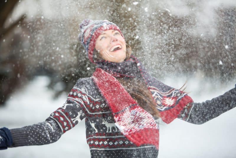 Lycklig ung kvinna som utomhus har gyckel på en snöig vinterdag
