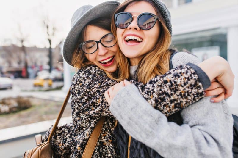 Lyckliga ljusa positiva ögonblick av två snygga flickor som kramar på gatan i staden