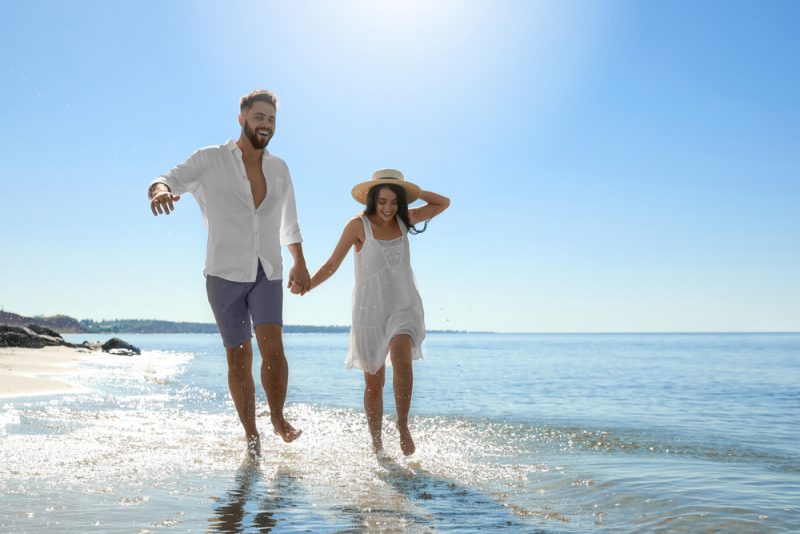 Lyckligt ungt par som kör på stranden nära havet