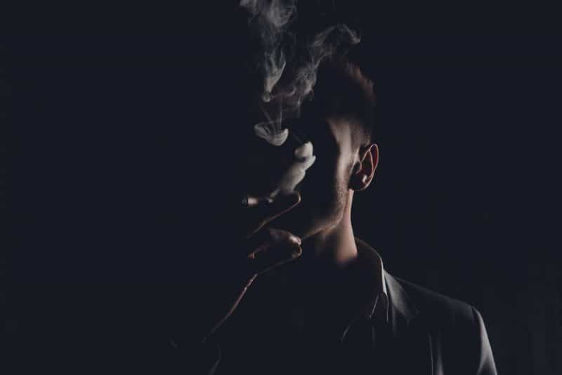 Mystikeman med cigarr och rök som isoleras på svart bakgrund
