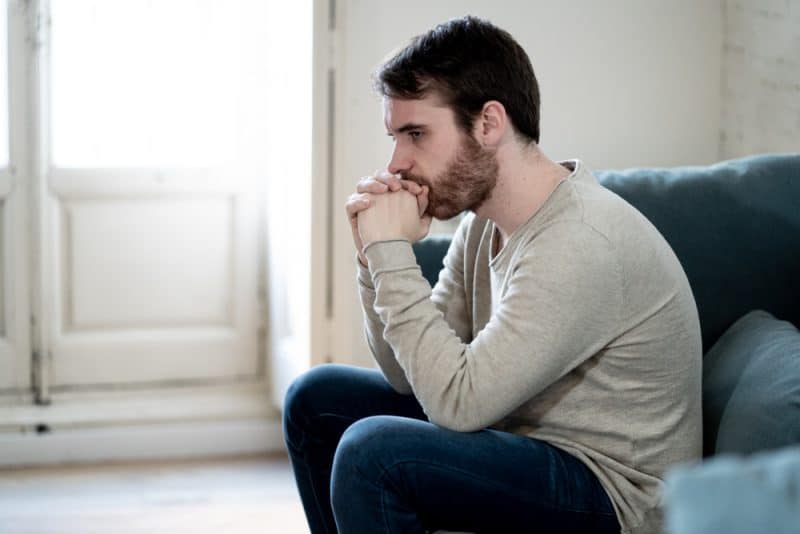 Olycklig deprimerad kaukasisk man som sitter och ligger i vardagsrum