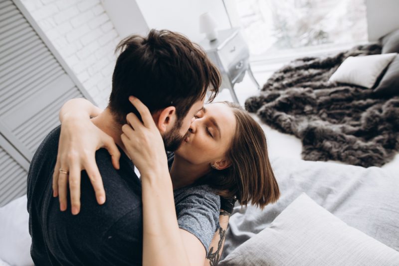 Paret som kysser på sängen i ett ljust rum