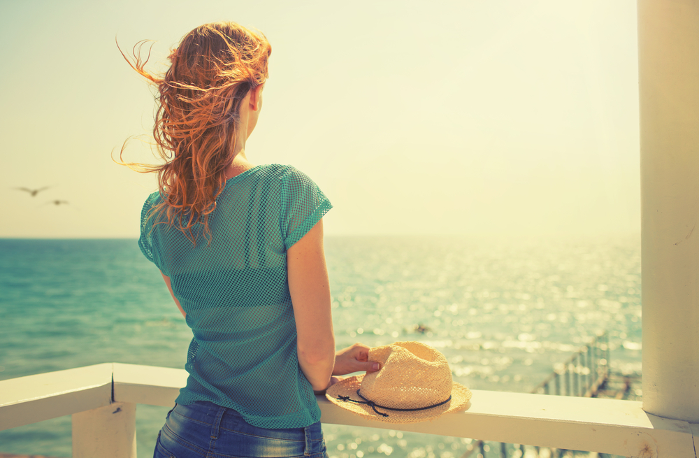 Ung flicka med hatten på staketet som ser havet