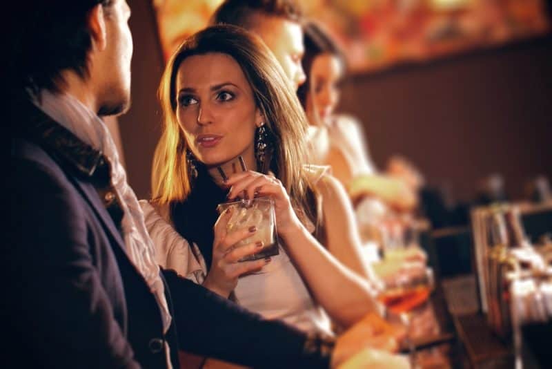 Ung kvinna med ett glas vin som talar till en man i baren