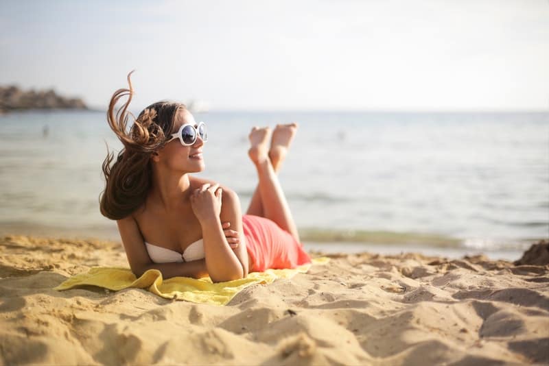 en le sexig kvinna med solglasögon som solar på en sandstrand