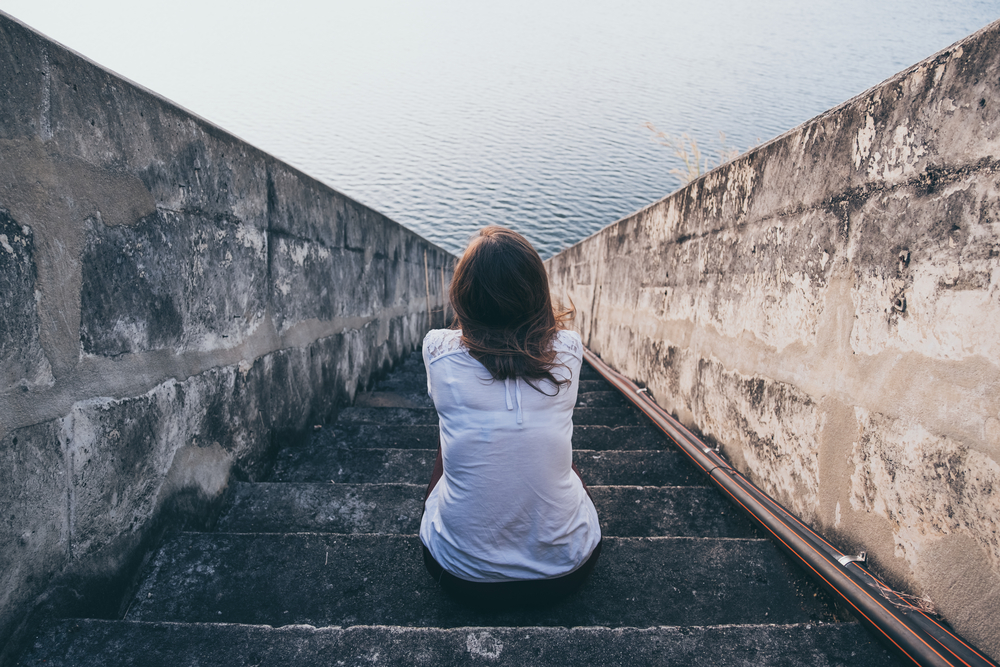 kvinna sitter på trappsteg och tittar på havet