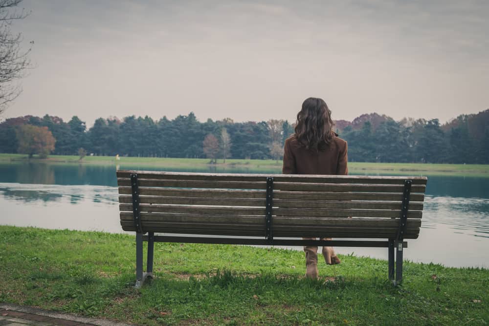 kvinna som sitter ensam på bänken nära sjön