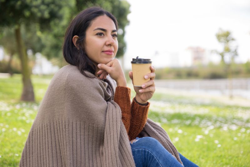 kvinna som sitter på gräset och dricker kaffe