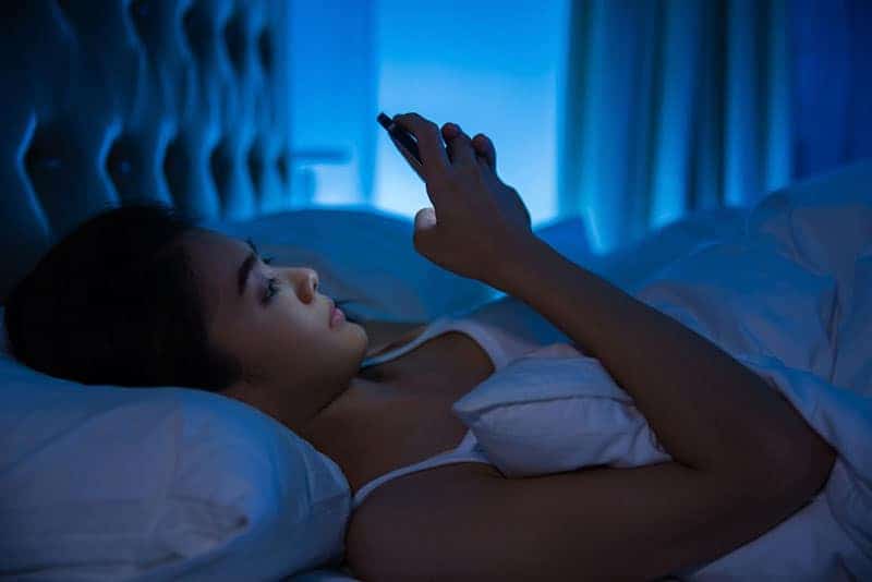 kvinna som skriver på sin telefon medan han ligger på sängen under natten