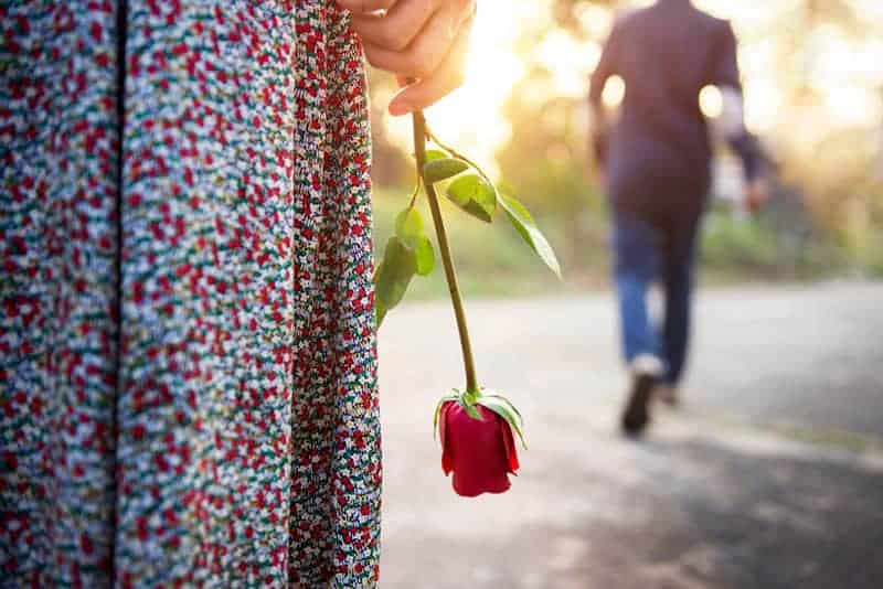 ledsen kvinna som håller en ros medan man lämnar