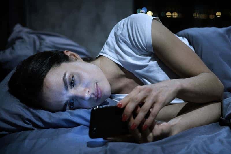 ledsen kvinna som tittar på telefonen i sängen
