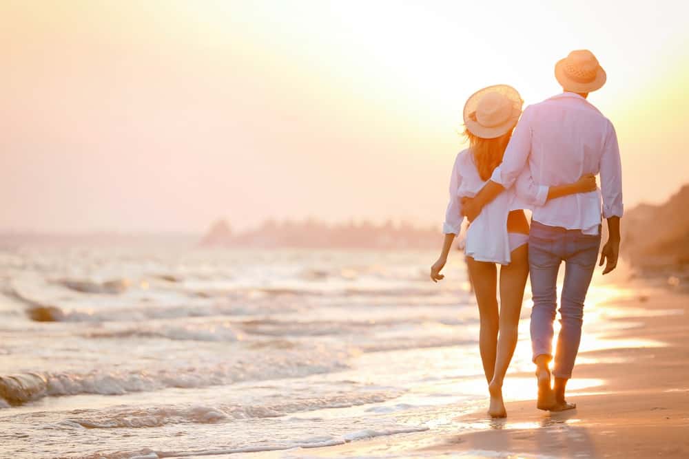 man och kvinna går tillsammans i solnedgången på stranden