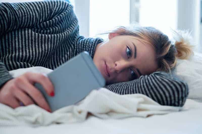 tankeväckande kvinna som ligger på sängen och skriver på sin telefon