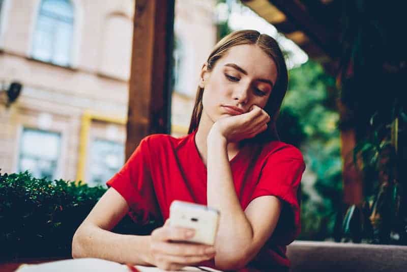 tankeväckande kvinna som bär röd t-shirt och tittar på sin telefon i café