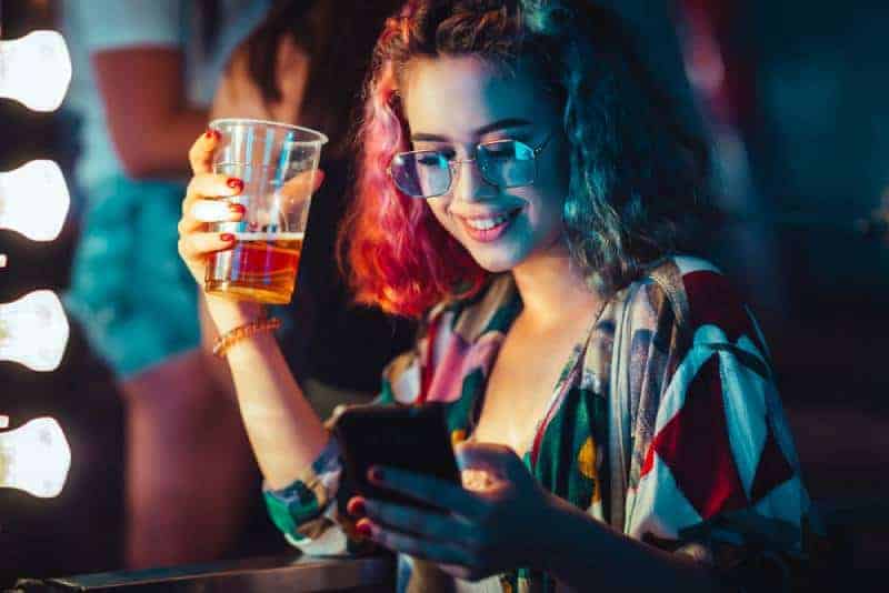 ung kvinna som dricker öl och skriver på sin smartphone