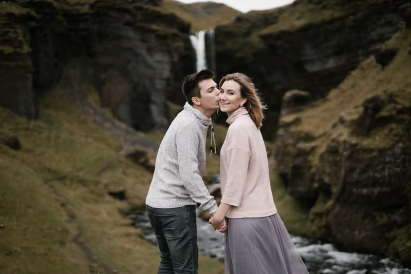 ute nära vattenfallet kysser en man en leende kvinna i ansiktet