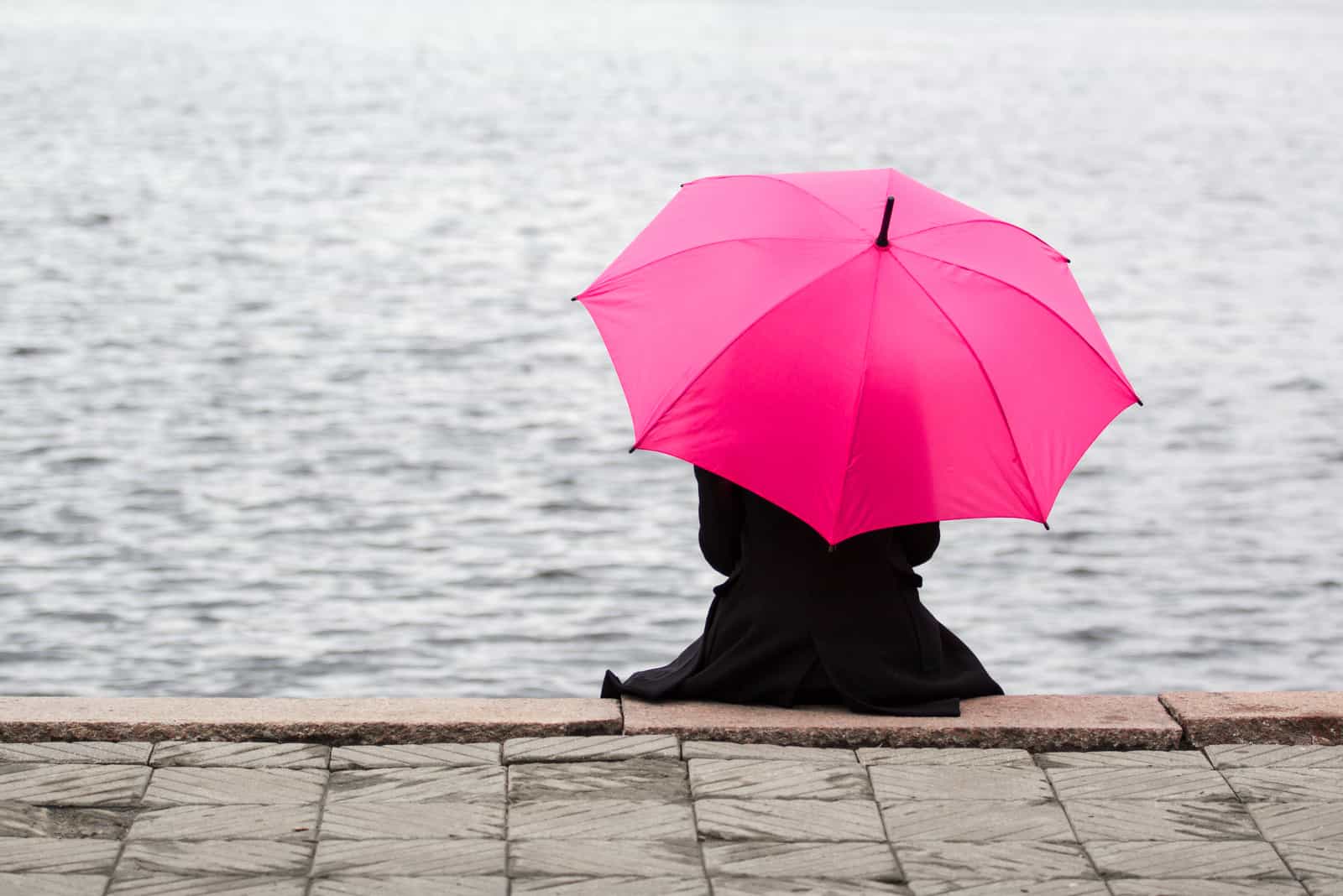 Kvinna som sitter ensamt med det rosa paraplyet