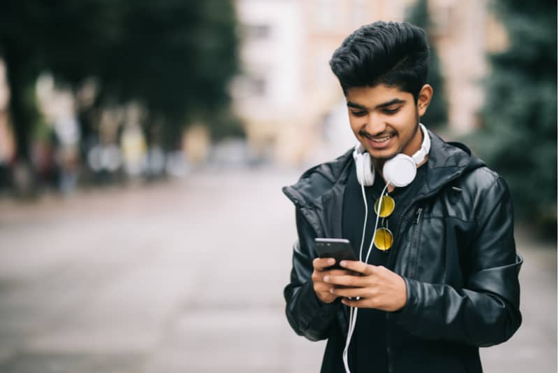 en glad ung man i en skinnjacka står på gatan och använder en mobiltelefon