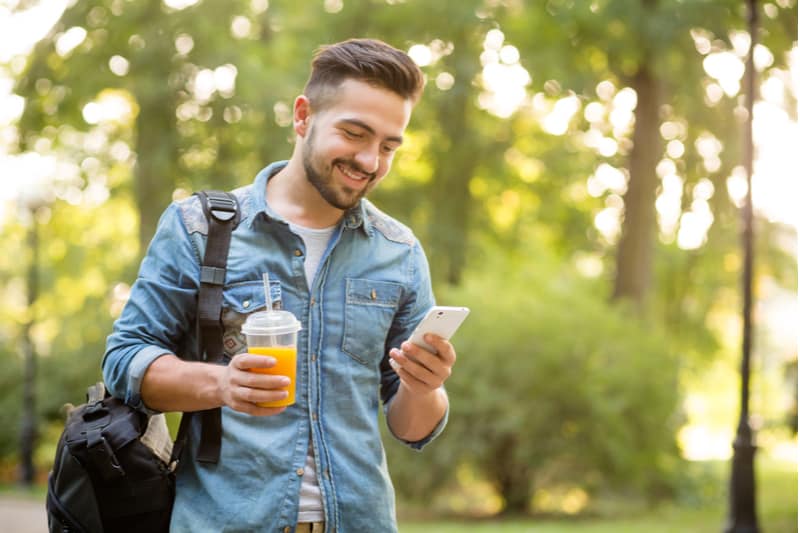 en leende man i en jeansjacka går förbi och använder en smartphone