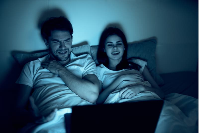 en man och en kvinna ligger i sängen och tittar på en film på en bärbar dator