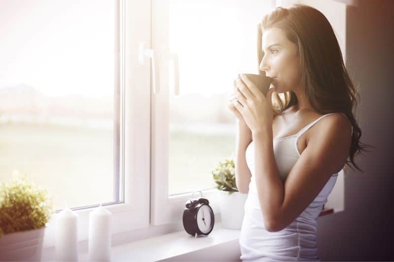 kvinna som dricker kaffe och tittar utanför fönstret