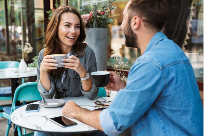 på caféets terrass sitter ett ungt leende par och dricker kaffe och pratar