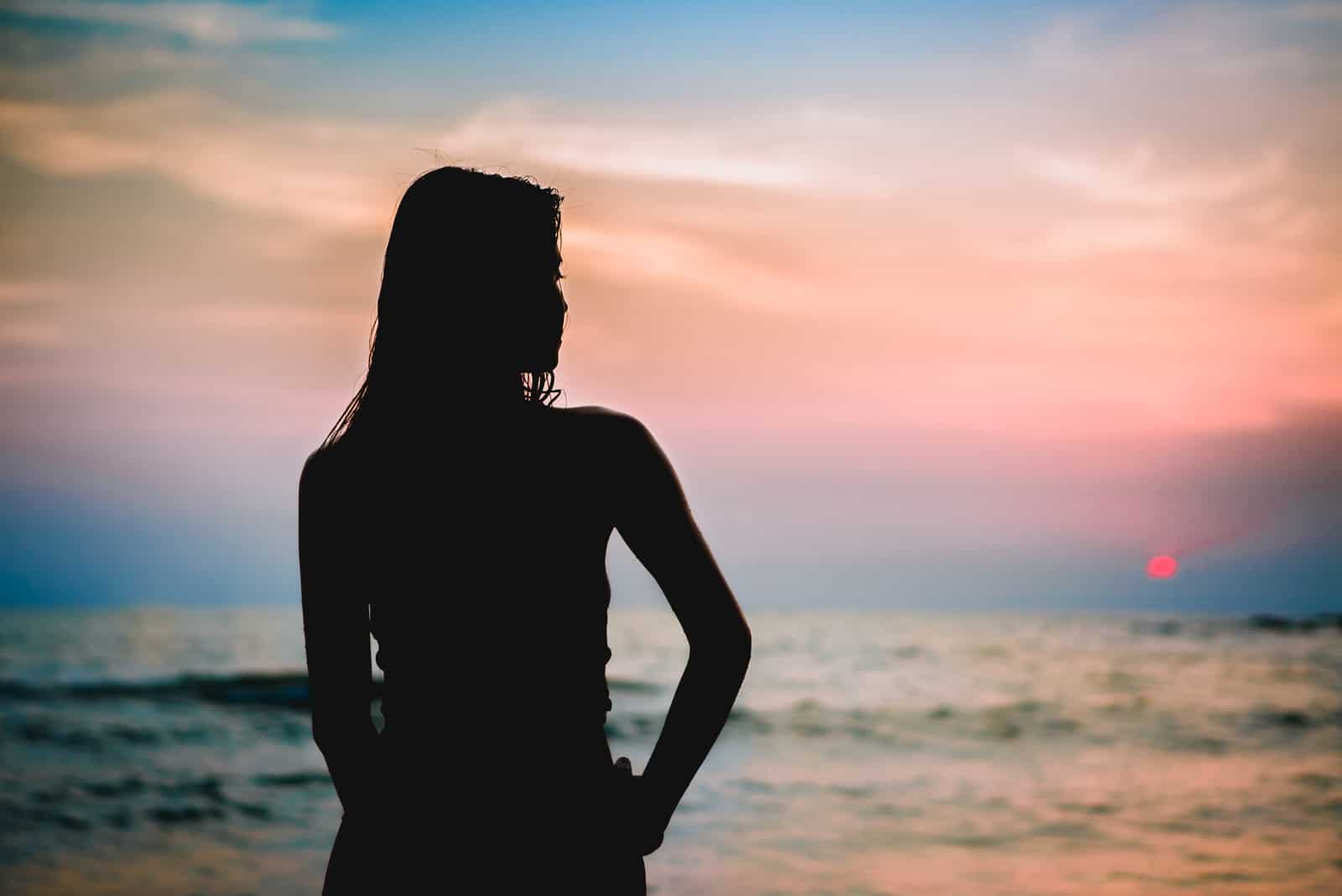 Ung kvinna för svart kontur som stirrar in i havet