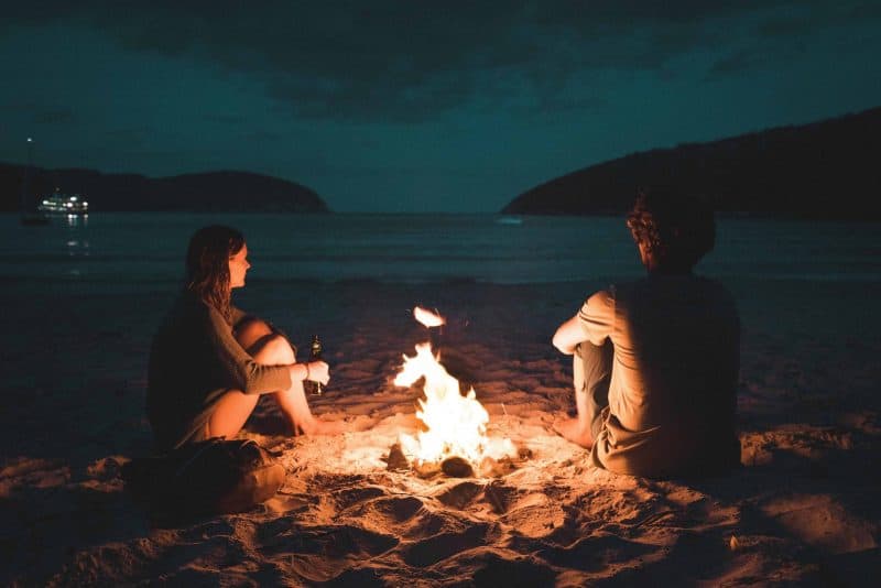 par som sitter på stranden nära eld