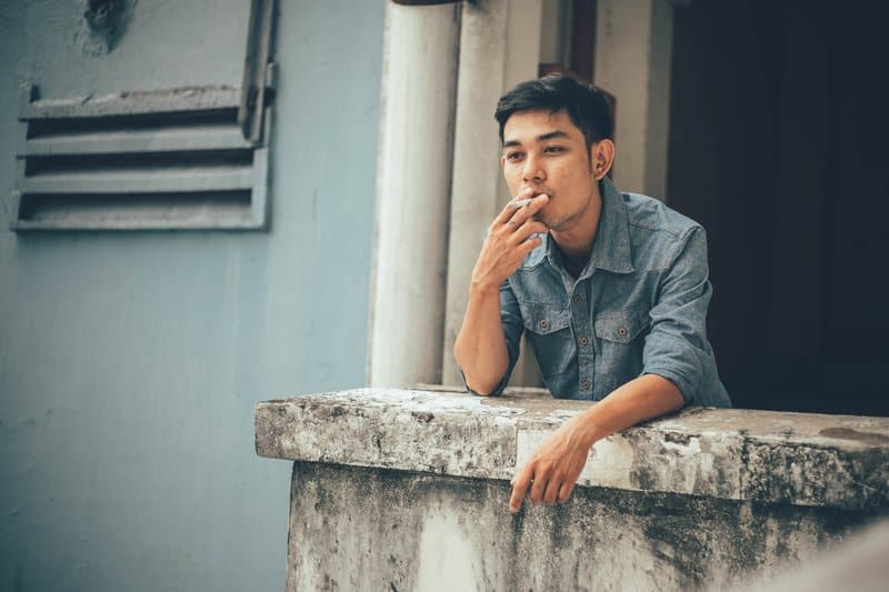 tankeväckande asiatisk man röker cigarett på balkongen
