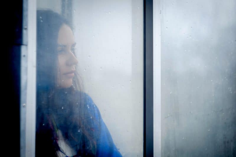 kvinna som bor nära fönstret och tittar på regndroppar