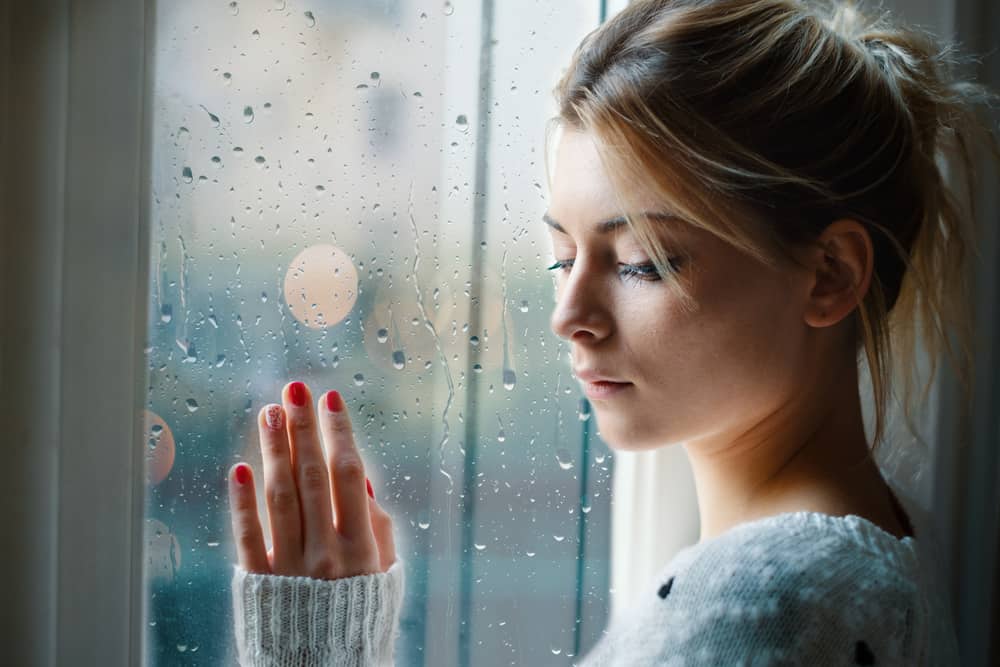 Ung flicka som ser ut genom fönstret på en regnig dag