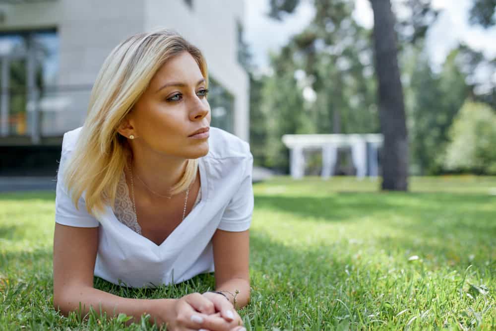 eftertänksam blond kvinna som ligger på gräset